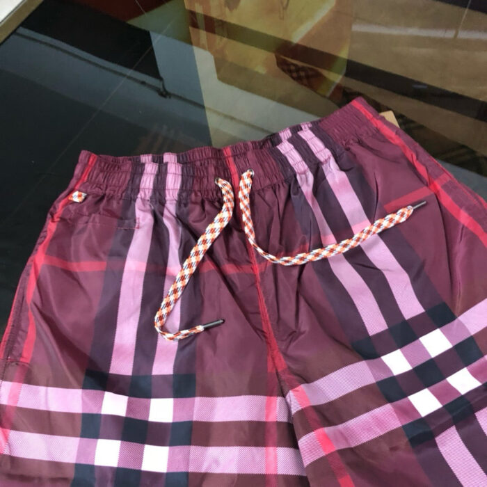 Pantaloncini da bagno a quadri rosso, rosa e nero con fascia elastica e laccio colorato.