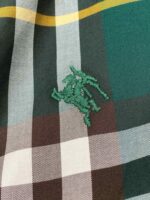 Tessuto a quadri verde, con ricamo logo sportivo, ideale per abbigliamento casual e raffinato.