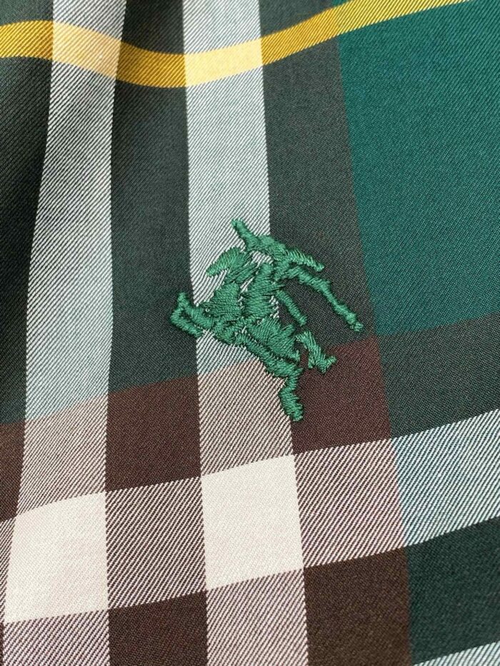 Tessuto a quadri verde, con ricamo logo sportivo, ideale per abbigliamento casual e raffinato.