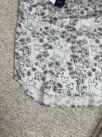 Maglietta azzurra con disegni di cani e fioretti artistici, perfetta per uno stile allegro e casual.