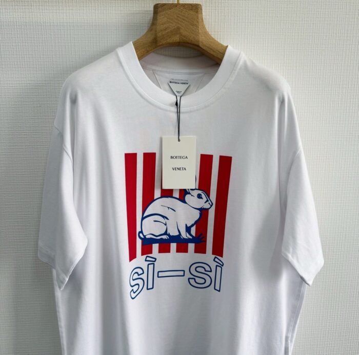 T-shirt bianco con gatto stilizzato, strisce rosse e scritta si-si in blu, stile giovane.