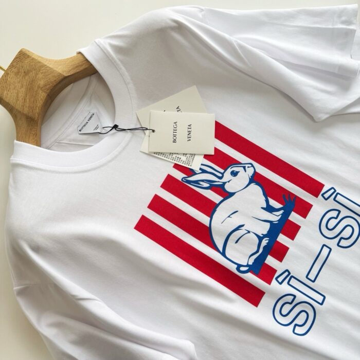 T-shirt bianca con grafica di coniglio stilizzato, strisce rosse e dettagli di marca.