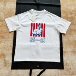 T-shirt bianco con coniglio colorato e dettagli a strisce rosse e bianche.
