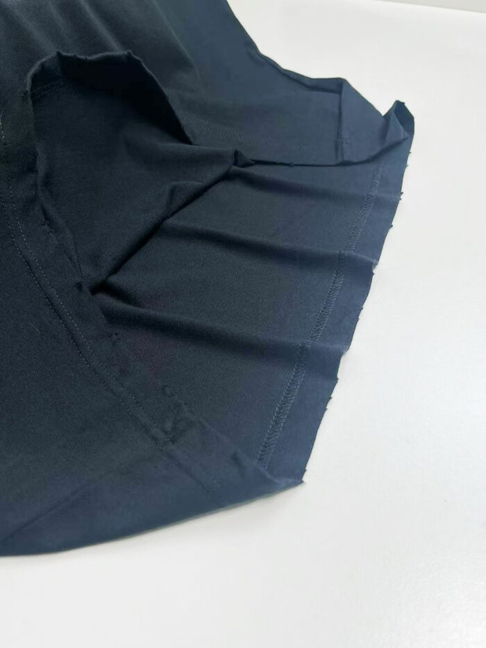 Dettaglio di una maglietta nera con pieghe e cuciture di alta qualità.