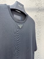 T-shirt nera Prada con logo triangolare in metallo, stile elegante e versatile per ogni occasione.