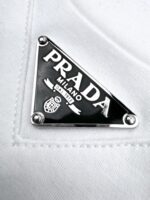 Logo Prada in metallo nero su tessuto bianco di lusso e dettagli raffinati.