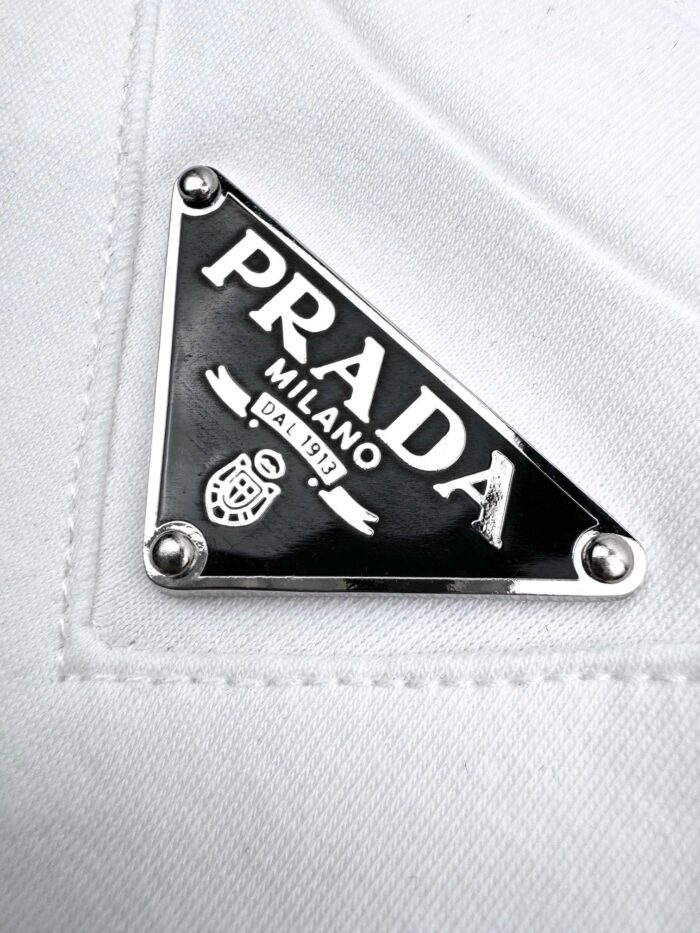 Logo Prada in metallo nero su tessuto bianco di lusso e dettagli raffinati.