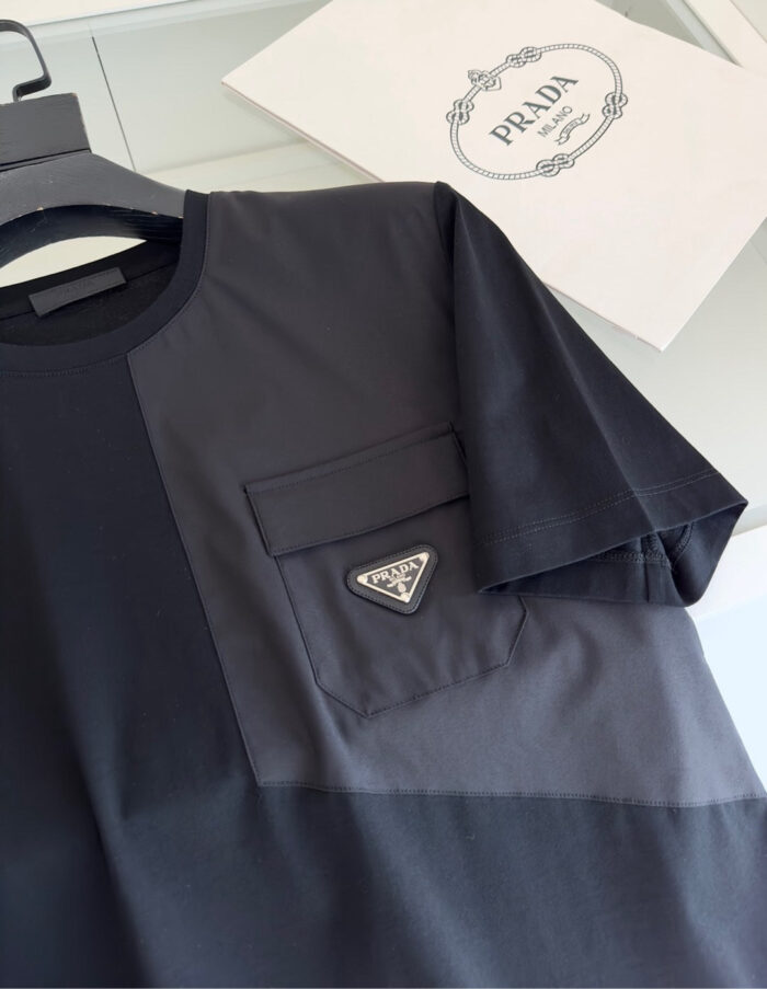 Maglietta Prada nera e grigia con logo e tasca moderna, ideale per uno stile elegante e casual.
