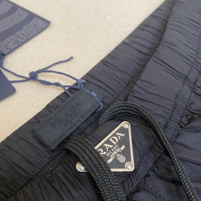 Pantaloni Prada navy con dettaglio pieghe e logo argentato, tessuto textured e confortevole.