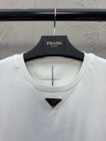 Maglietta bianca Prada con logo triangolare elegante, design minimalista e stile di lusso sofisticato.