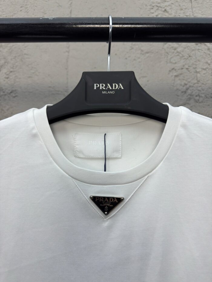 Maglietta bianca Prada con logo triangolare elegante, design minimalista e stile di lusso sofisticato.