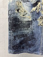 Jeans distressed con graffiti e messaggi ribelli, stile streetwear e arte urbana.