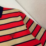 Polo Prada a righe rosso e beige con colletto navy, stile elegante e casual.