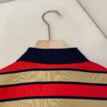 Camicia a righe rossa, beige e navy, stile casual sportivo su hanger di legno.