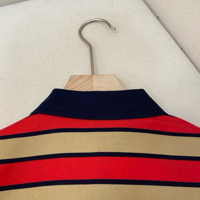 Camicia a righe rossa, beige e navy, stile casual sportivo su hanger di legno.