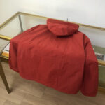 Giacca rossa elegante in esposizione su tavolo di legno e vetrina di boutique raffinata.