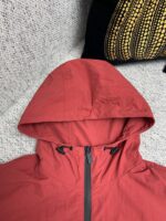 Giacca rossa da esterno con cappuccio regolabile, dettagli pratici e stile outdoor.