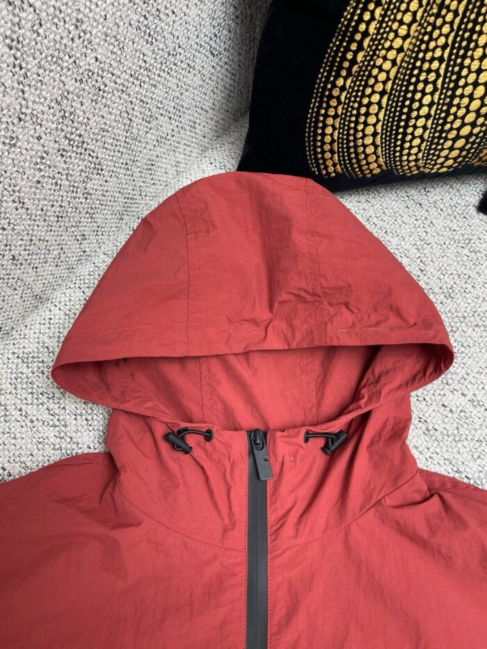 Giacca rossa da esterno con cappuccio regolabile, dettagli pratici e stile outdoor.
