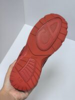 Scarpa sportiva con suola rossa antiscivolo, mostrata in mano, design ergonomico e grip efficace.