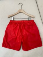 Pantaloncini estivi rossi su attaccapanni in legno, stile casual e sportivo.