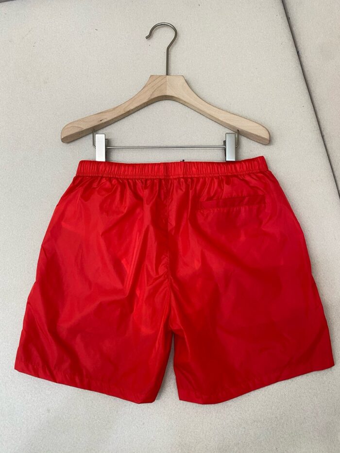Pantaloncini estivi rossi su attaccapanni in legno, stile casual e sportivo.