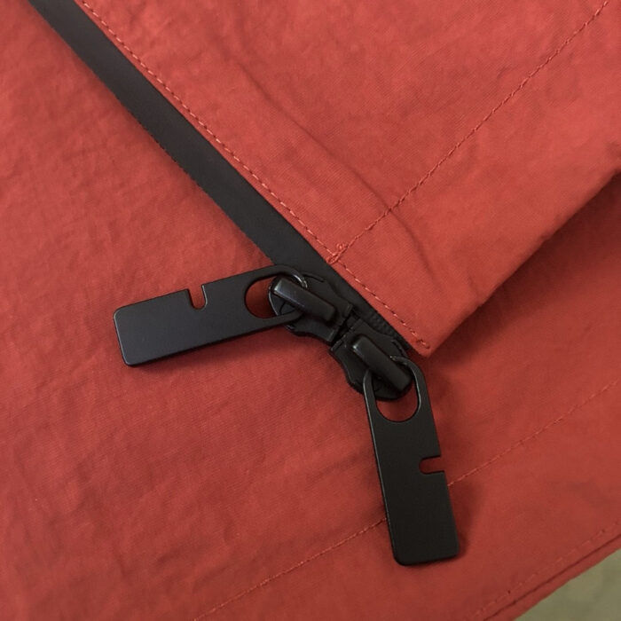 Dettaglio di una moderna zip nera su tessuto rosso arancione vibrante.