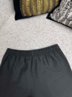 Pantaloni neri casual, ambientazione accogliente con cuscini decorativi e atmosfera relax in casa.