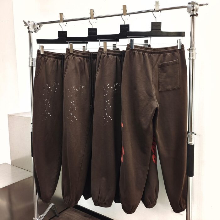 Pantaloni marroni moderni con dettagli artistici su stendibiancheria minimalista in ambiente neutro.