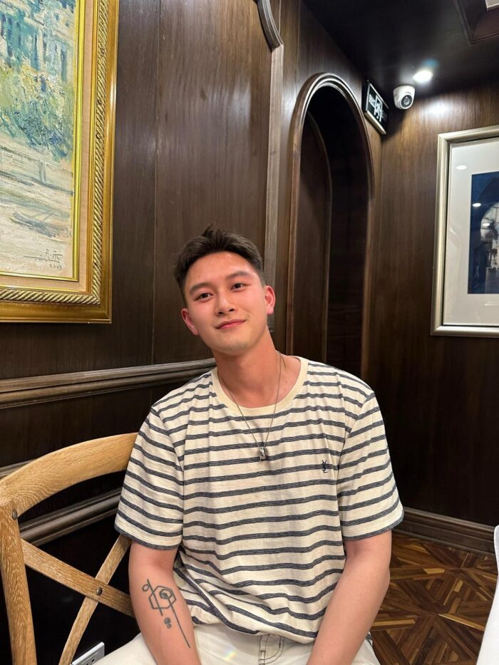 Giovane uomo sorridente in ambiente elegante con legno scuro e decorazioni artistiche.