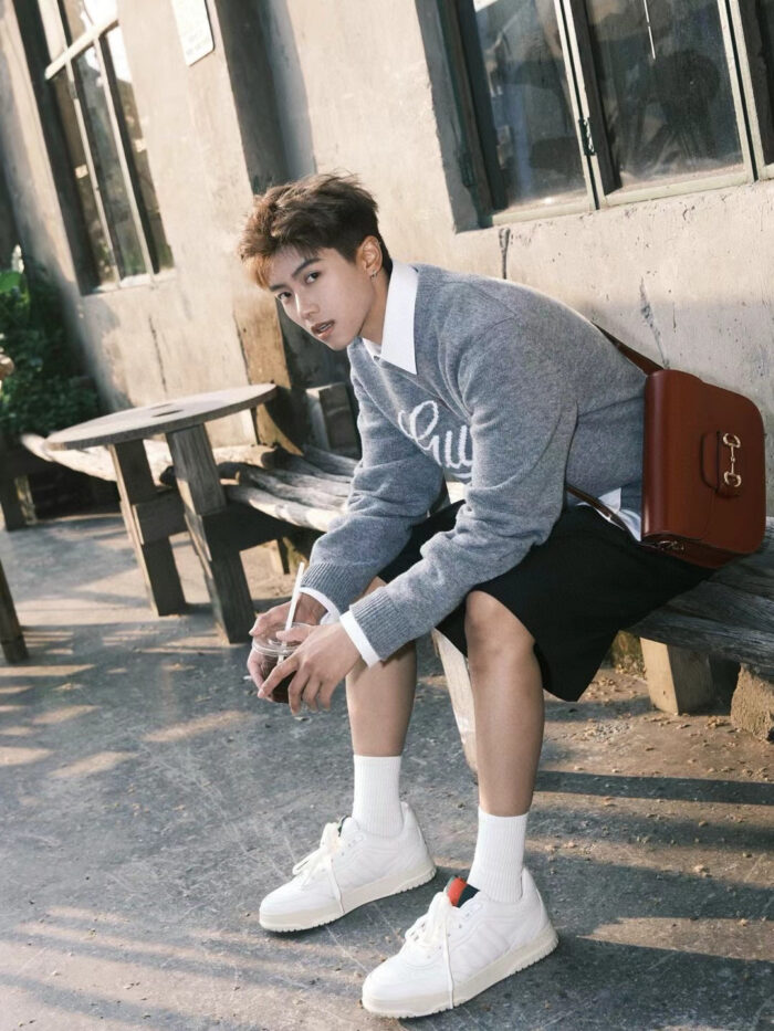 Ragazzo giovane in stile casual con earbuds, seduto in ambientazione urbana e rilassato.