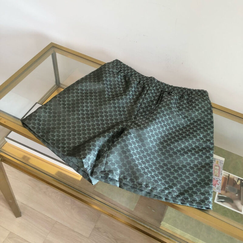 Pantaloncini geometrici moderni in tessuto leggero su tavolino in vetro e dorato.