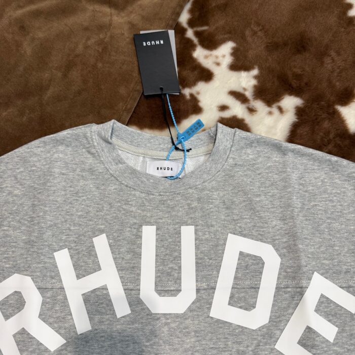 Felpa grigia Rhude con logo bianco, tag di sicurezza, stile streetwear elegante e confortevole.