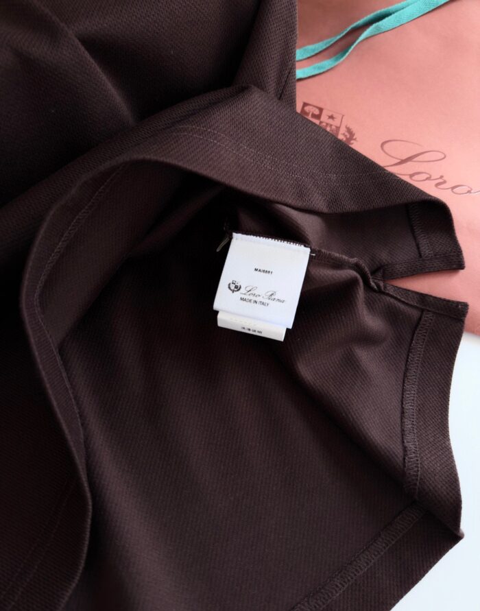 Dettaglio di abbigliamento marrone con etichetta e confezione rosa con nastri turchesi.