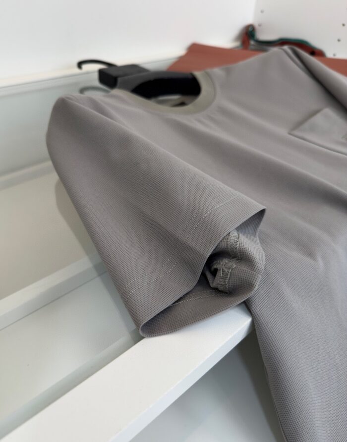 Manica di camicia grigia arrotolata su mensola, in ambiente minimalista e ben organizzato.