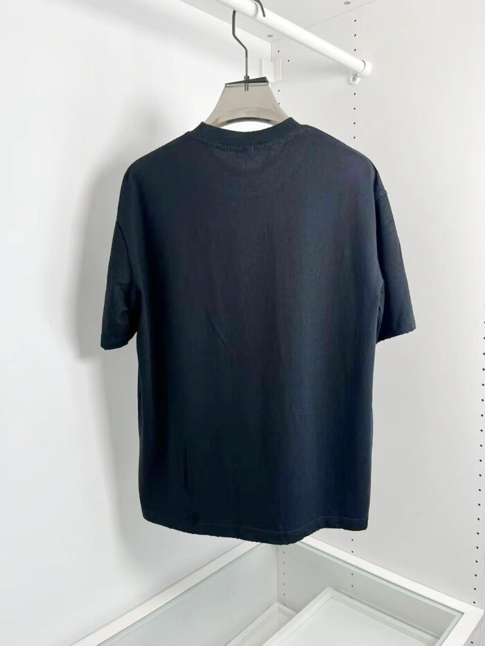 Maglietta nera classica, semplice e versatile, appesa su gruccia in ambiente minimalista.