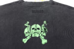 Maglietta nera con grafica di tre teschi verdi e croci dal design distressed, stile punk-rock.