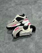 Scarpe sportive moderne in suede beige, nero e dettagli rosa su superficie grigia.