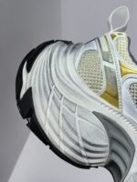Sneaker atletica moderna bianca con dettagli oro, suola nera e design dinamico per stile e performance.