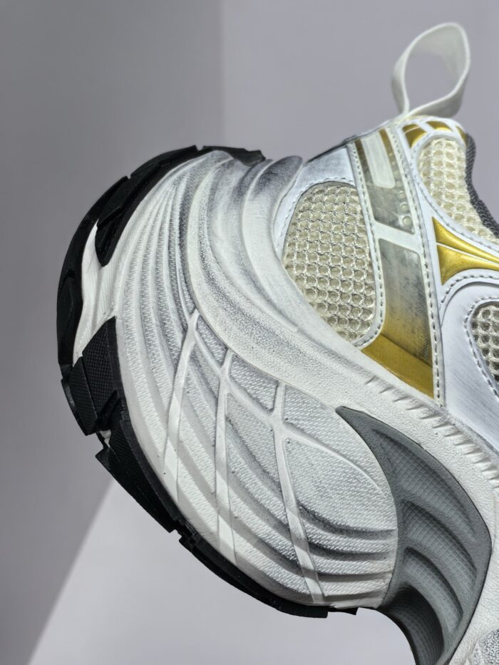 Sneaker atletica moderna bianca con dettagli oro, suola nera e design dinamico per stile e performance.