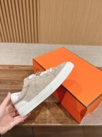 Sneaker beige in suede con scatto bianco e scatola arancione elegante, stile moderno e raffinato.