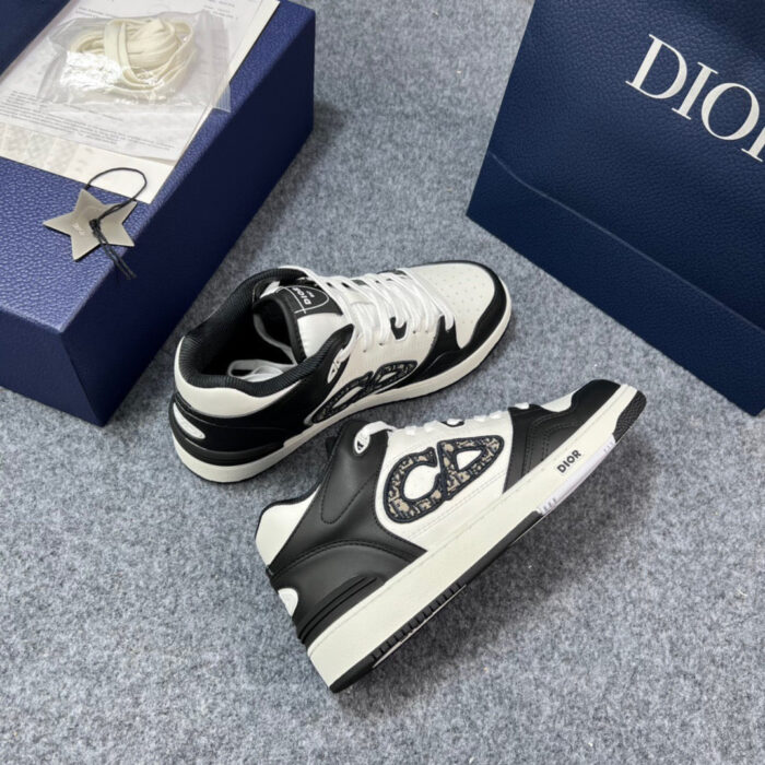 Sneakers nere e bianche di lusso con logo, presentate su scatola blu e charm argentato.