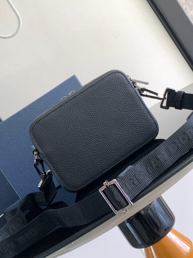 Borsa nera compatta in pelle con manico metallico e confezione blu elegante.