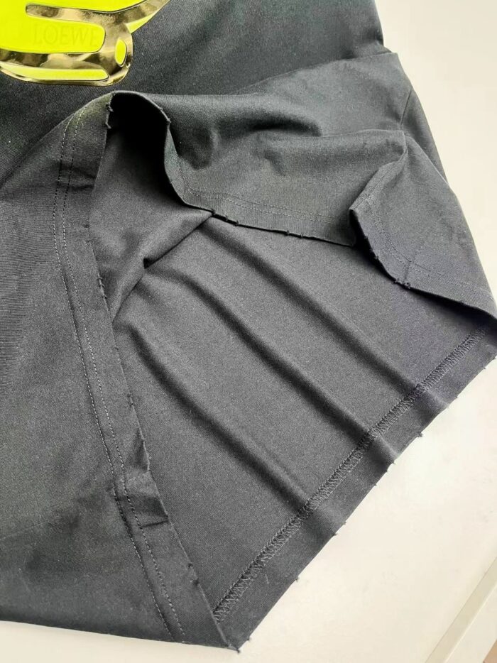 Maglietta nera con pieghe, logo giallo e dettagli eleganti, stile moderno e versatile.