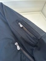 Giacca nera moderna con tasche zippate, ideale per stile casual e attività allaperto.