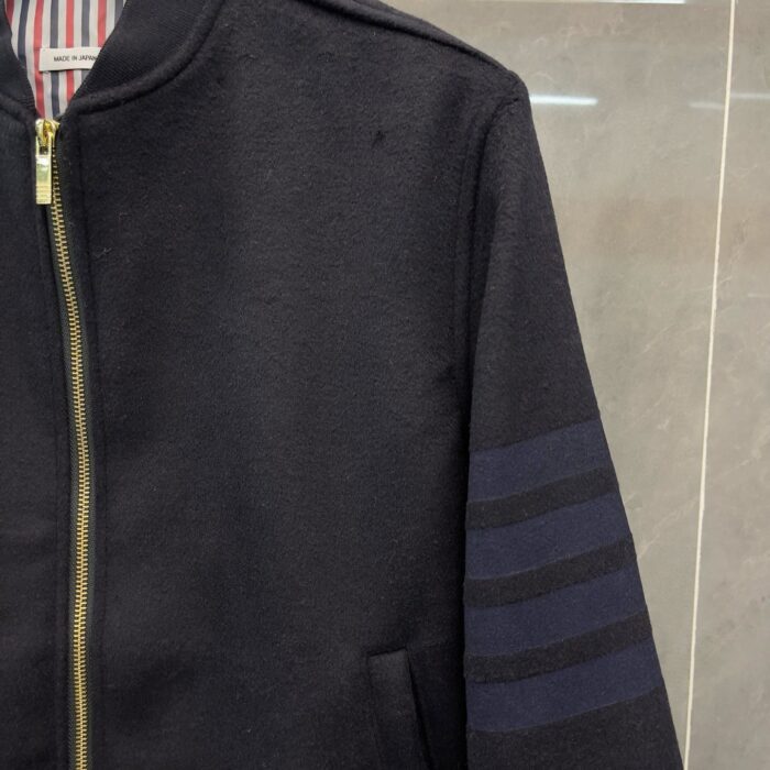 Giacca bomber nera con strisce sportive, zip dorata e interno a righe rosse e bianche.