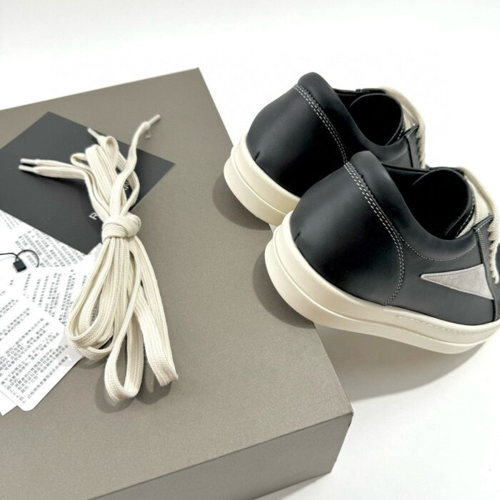 Sneakers nere in pelle minimaliste con lacci off-white, eleganti e moderne, su scatola grigia opaca.