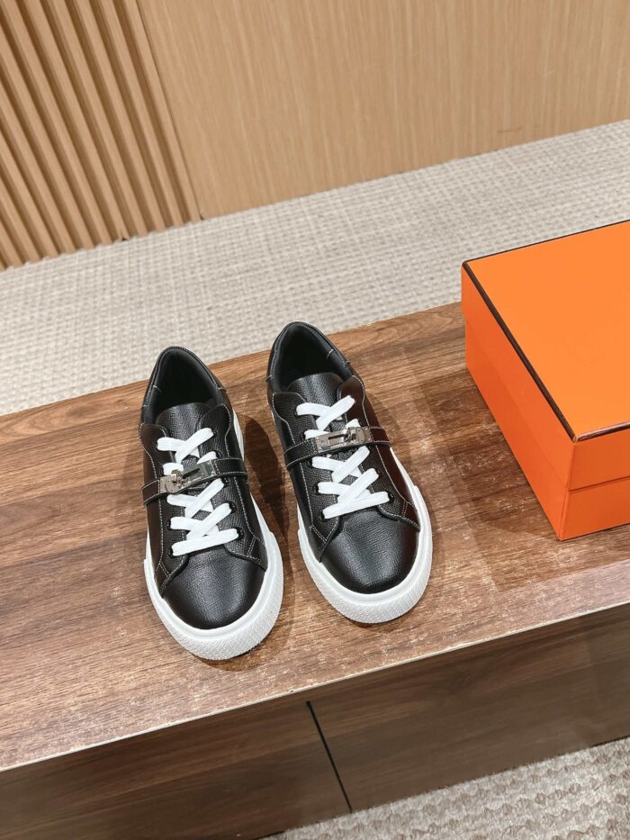 Sneakers nere in pelle con lacci bianchi su superficie di legno, scatola arancione, stile elegante.
