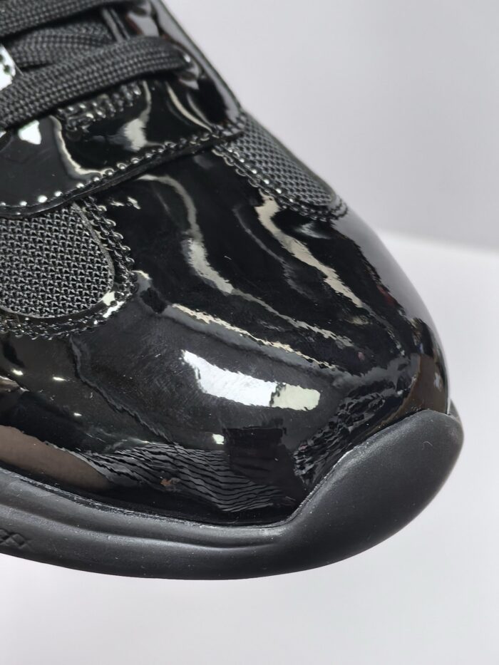 Sneaker nera lucida in pelle sintetica, design moderno, dettagli in mesh, stile elegante e sportivo.