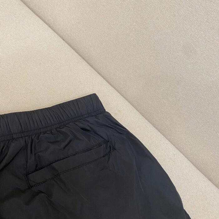 Pantaloncini da sport neri minimalistici su divano beige, comodi e leggeri, con tasca posteriore.