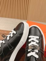 Scarpe sneakers nere in pelle con lacci bianchi e dettaglio metallico, su superficie in legno calda.